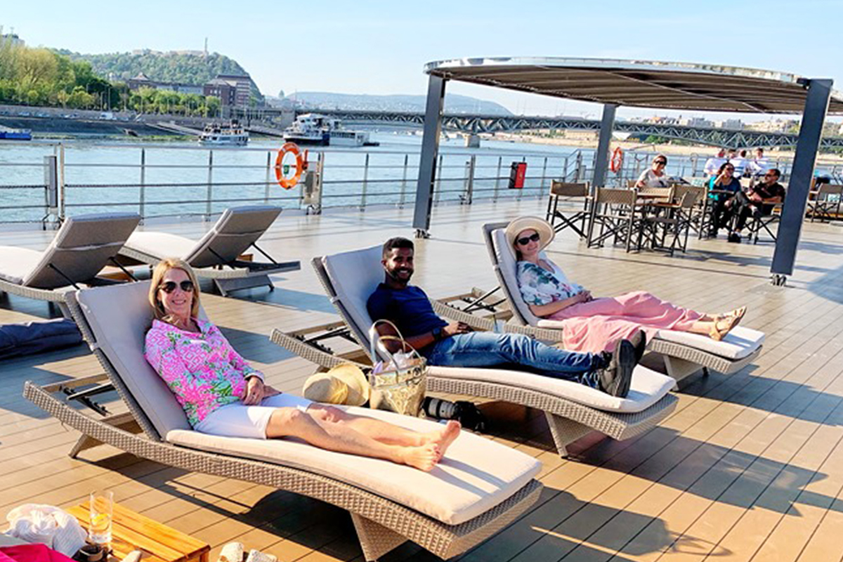 a man and woman sitting on lounge chairs on a deck by the water